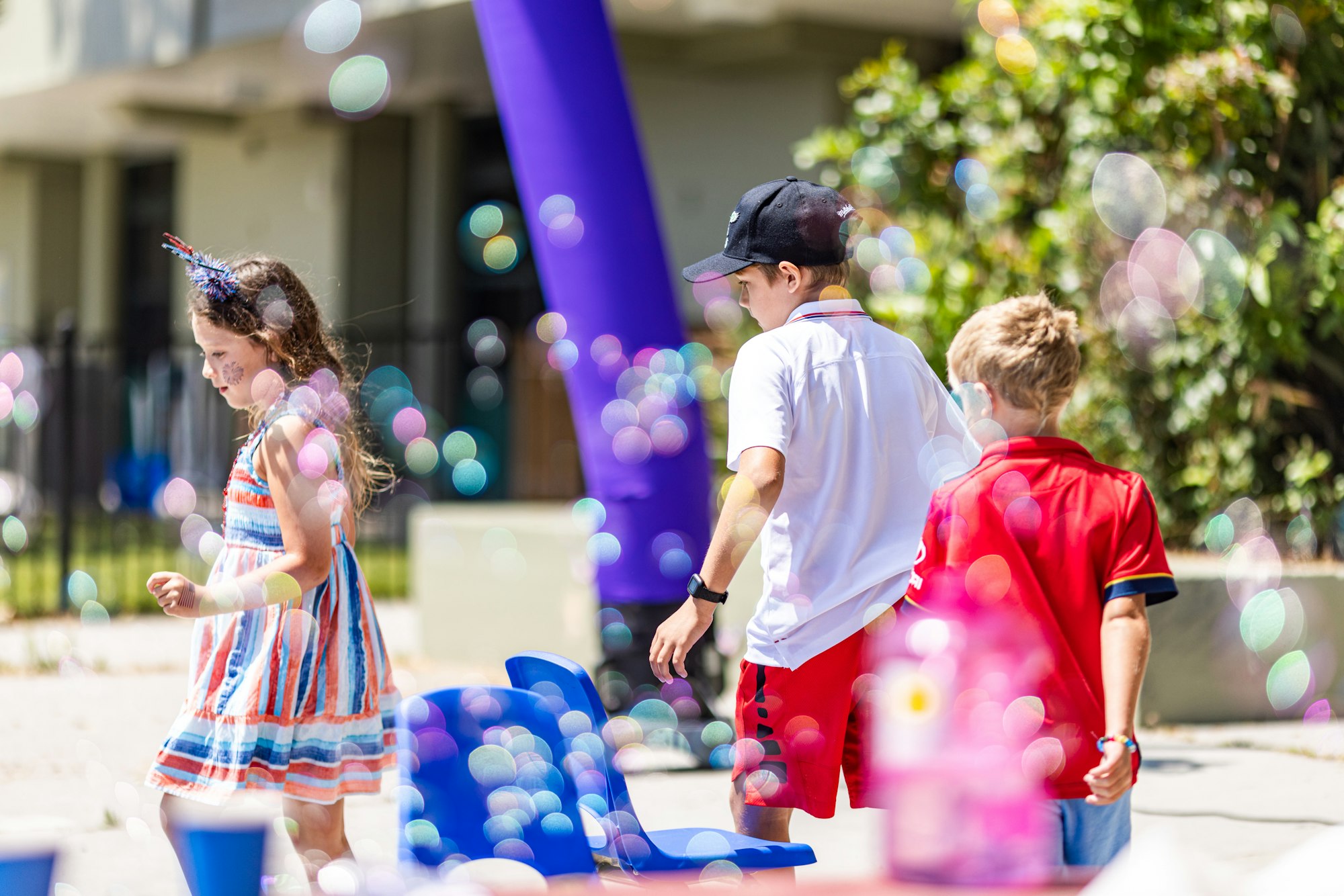 Children walking outdoors, surrounded by bubbles, in a colorful and playful setting.