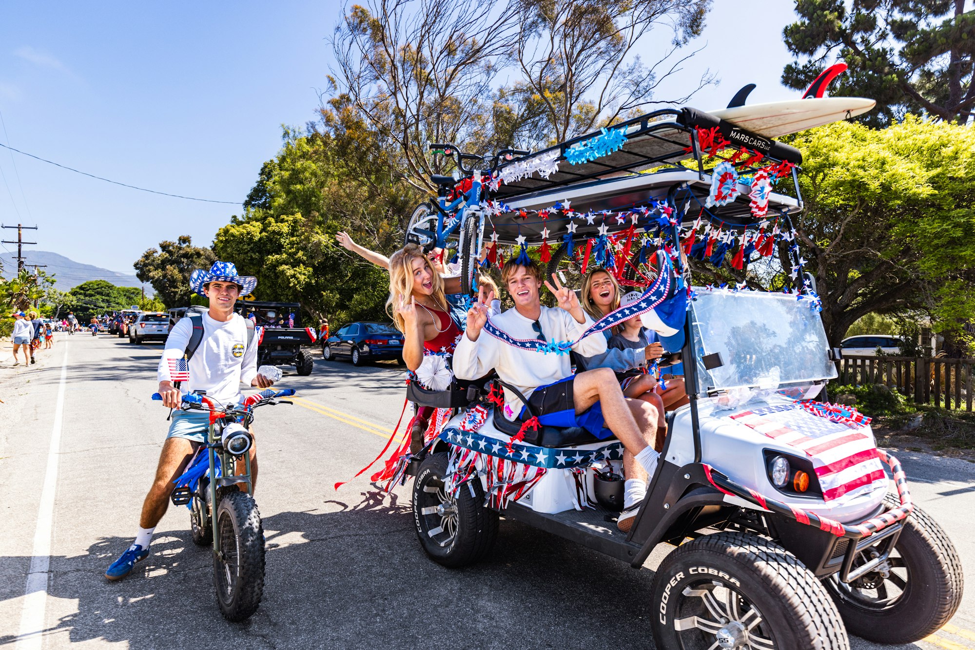People on a decorated golf cart and bike in a festive street parade.