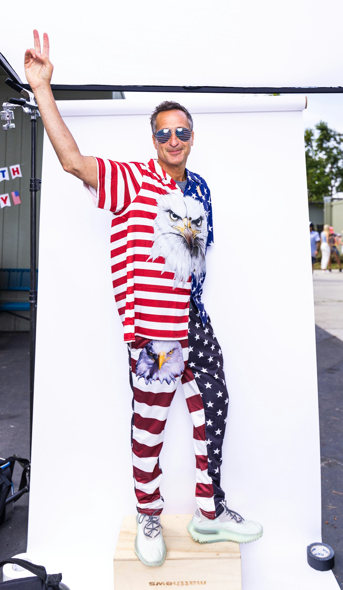 A person wearing a patriotic outfit with an eagle design and waving a peace sign.