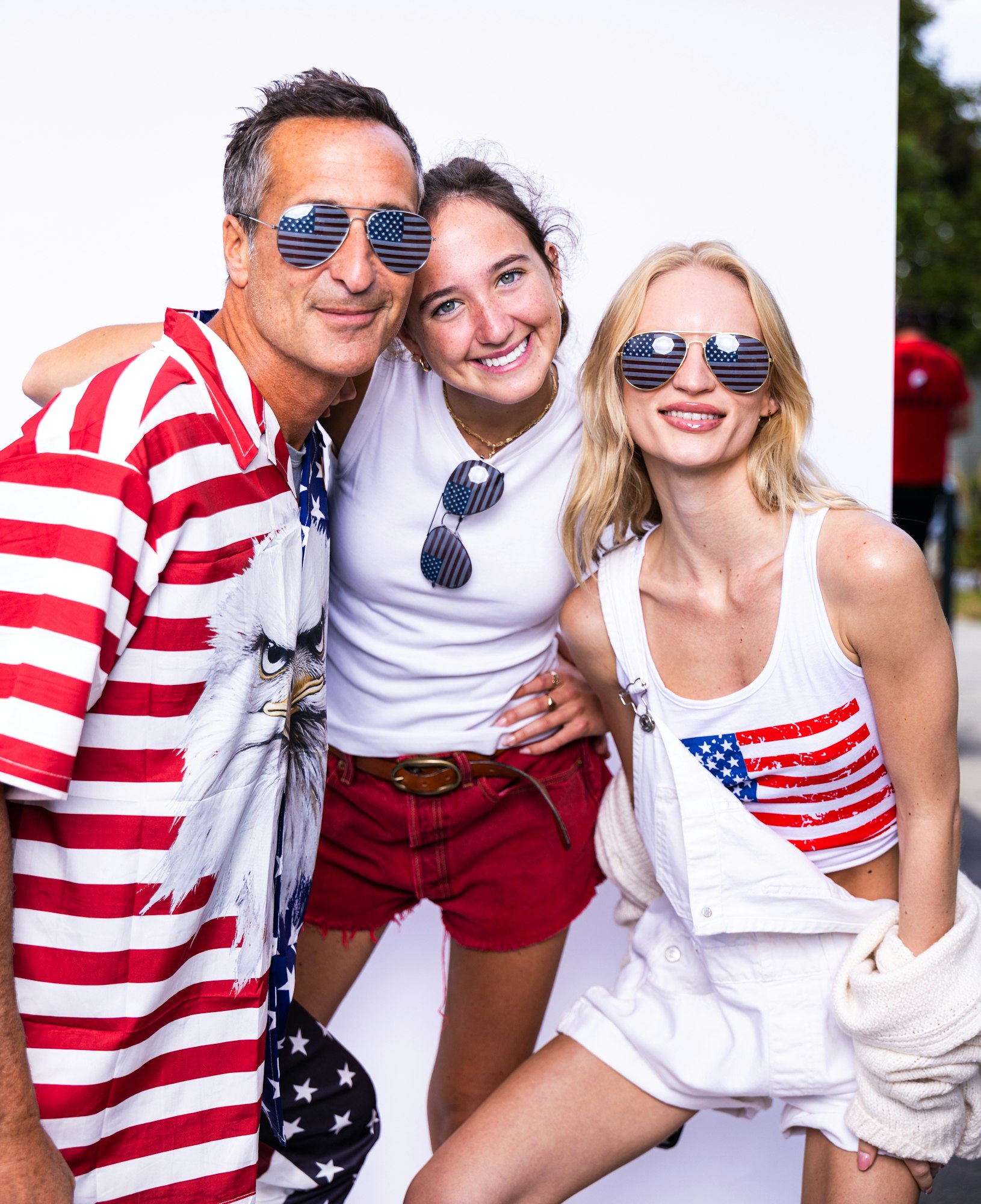 Three people wearing American flag-themed outfits and sunglasses, smiling at the camera.