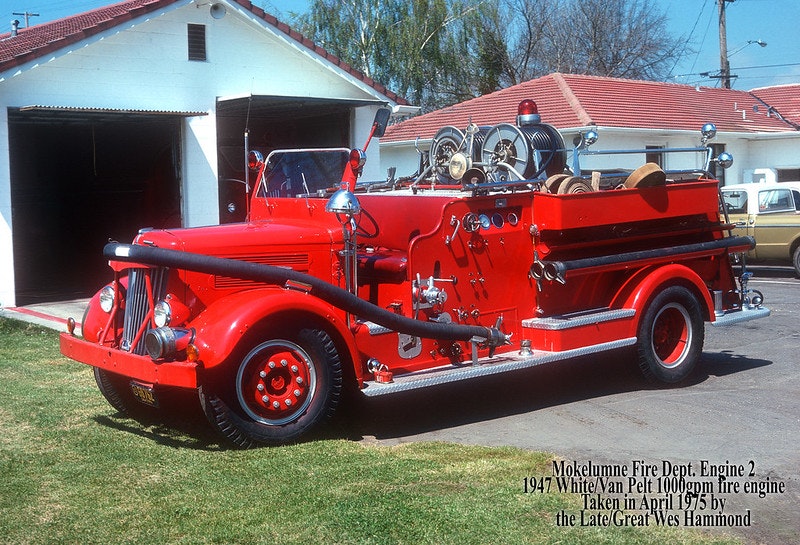 Vintage red fire engine parked outside with equipment on board.