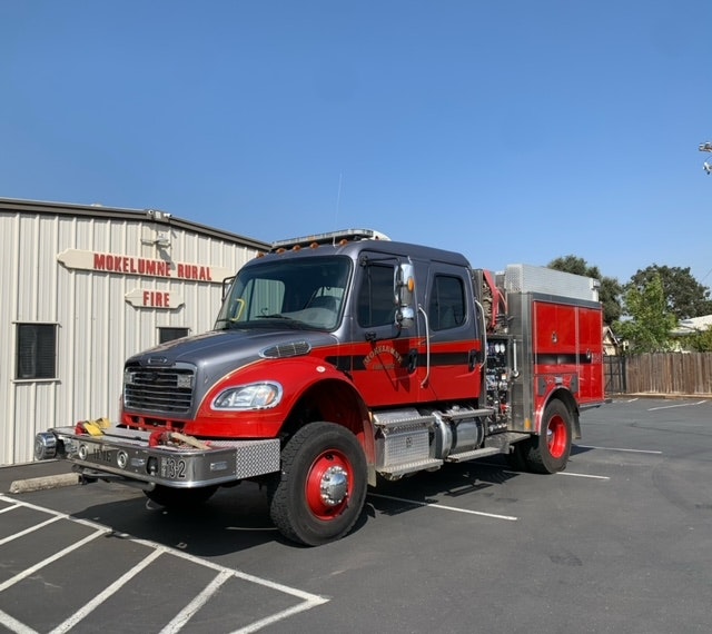 A red and silver fire truck parked outside the Mokelumne Rural Fire station on a clear day.