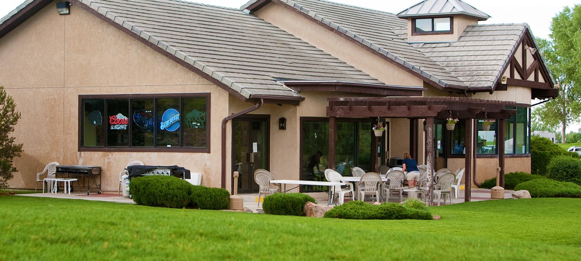 A building with a patio area, lawn chairs, and a grassy lawn, with neon beer signs visible in the window.