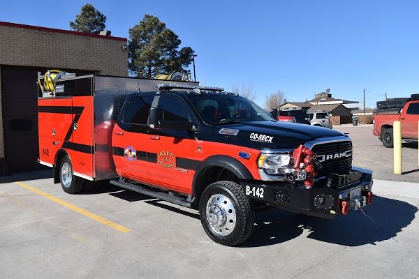 A red and black fire truck with a utility body, parked in a lot, featuring emergency equipment and signage.