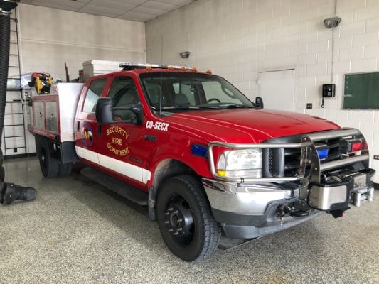 A red fire department vehicle, equipped for emergencies, parked inside a fire station with firefighting tools visible.