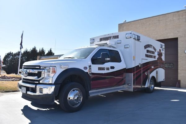 The image shows a white and red ambulance labeled "Security Fire" parked in front of a building.