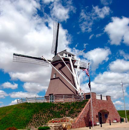 A traditional windmill under a blue sky with clouds, featuring an American flag.