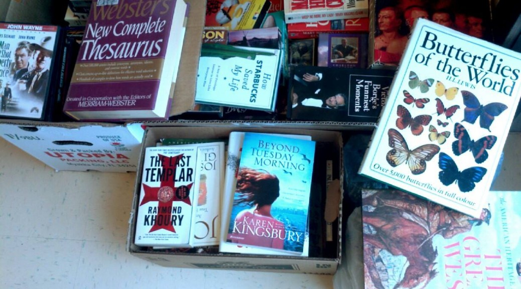 An assortment of books in cardboard boxes, including titles on butterflies, a thesaurus, and various novels.