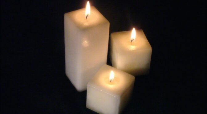 Three lit candles of varying heights against a dark background.