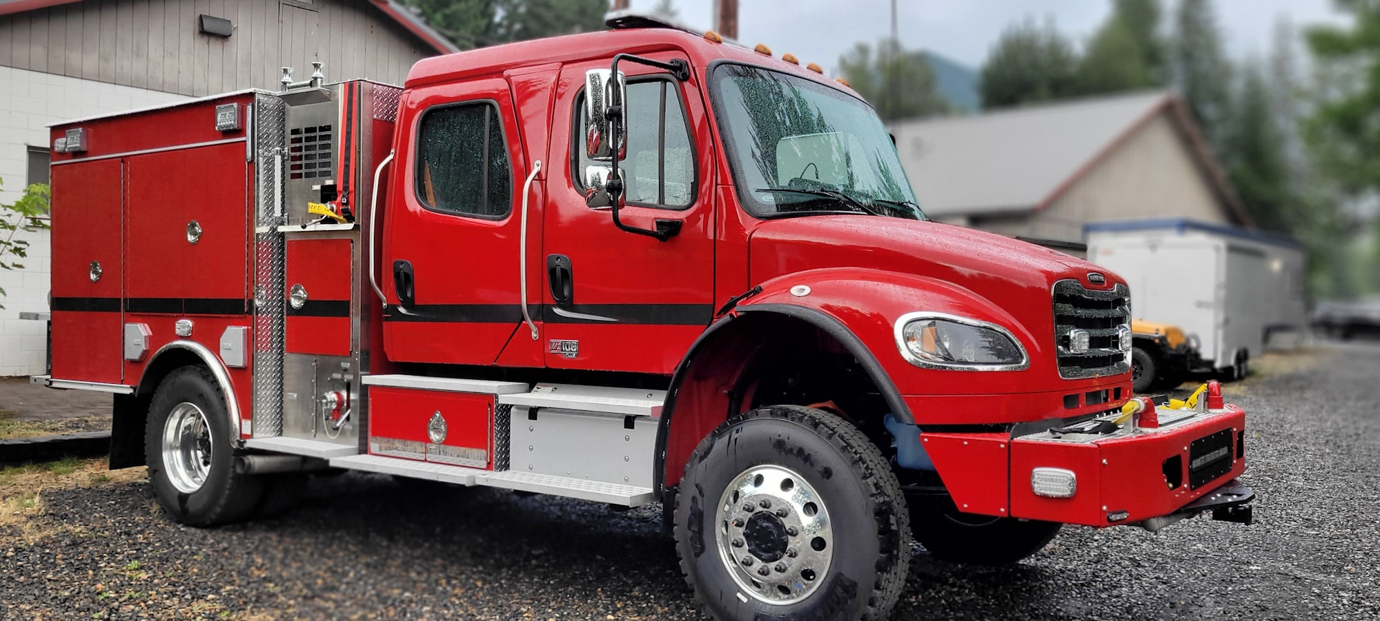 Red firetruck parked on a gravel lot with equipment compartments and a blurred background.