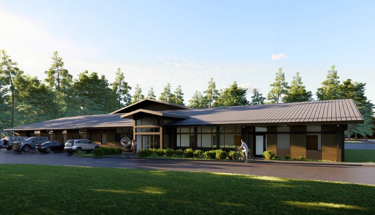 A modern building surrounded by trees, featuring large windows, a metal roof, and a manicured lawn, with a cyclist nearby.
