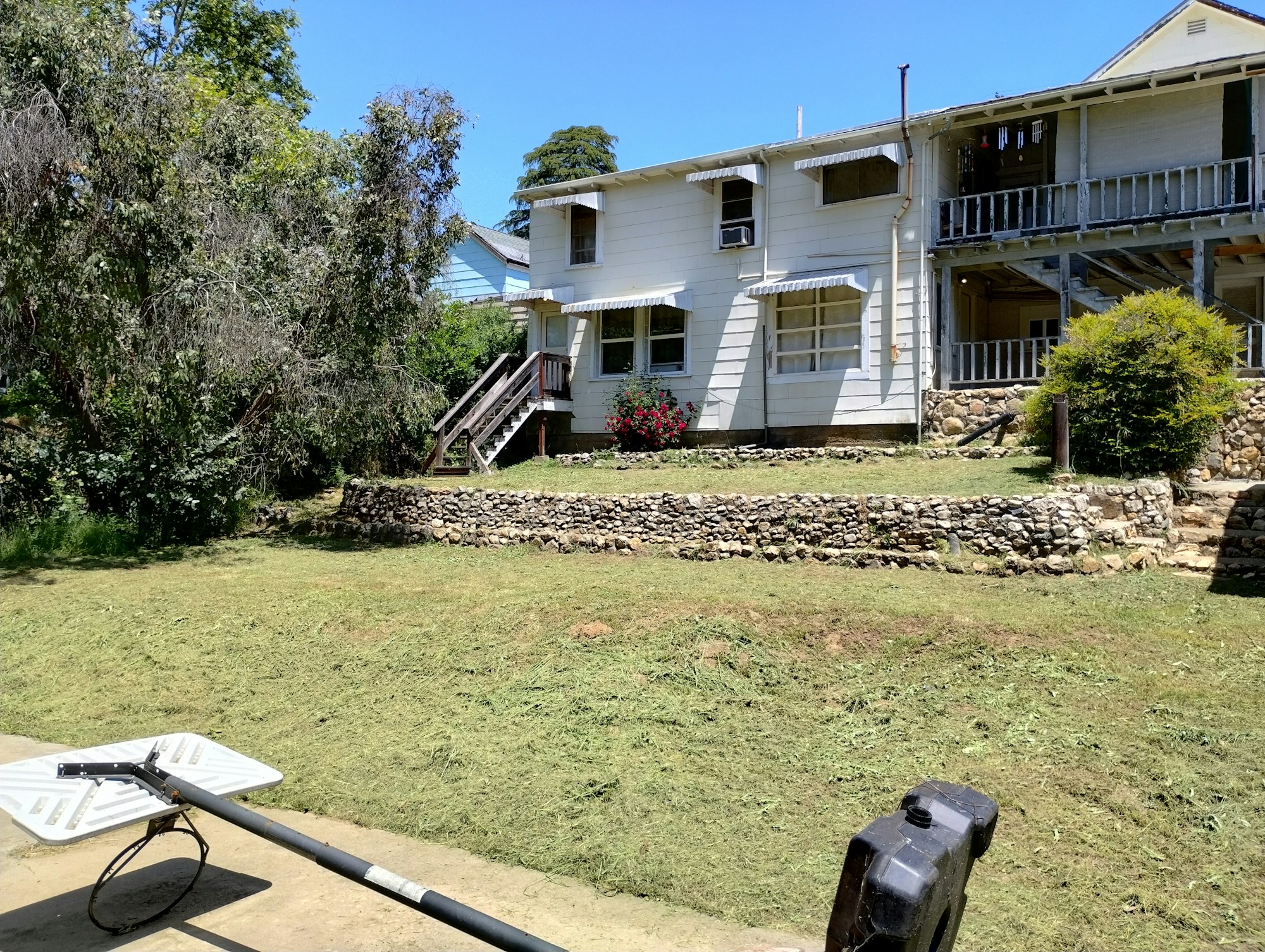 A two-story white house with a stone wall, surrounded by green trees and mowed grass, and a satellite dish in the foreground.