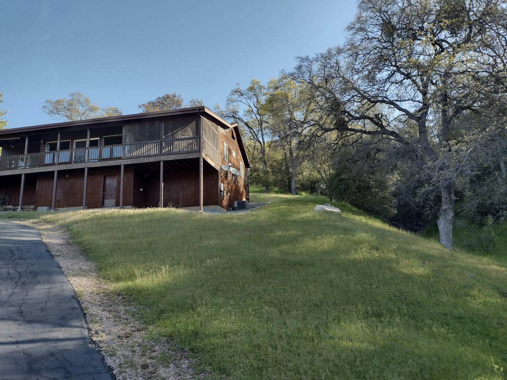 Wooden house on a grassy hill with trees, under a clear blue sky.