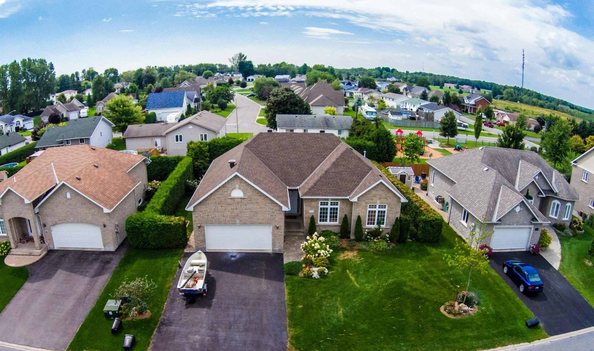 An aerial view of a suburban neighborhood featuring houses, greenery, playgrounds, and clear skies.