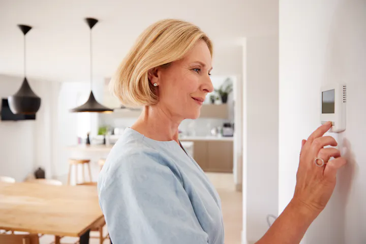 A woman adjusts a thermostat in a modern kitchen.