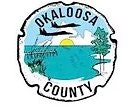 Seal of Okaloosa County featuring coastline, trees, planes, and a sunrise.