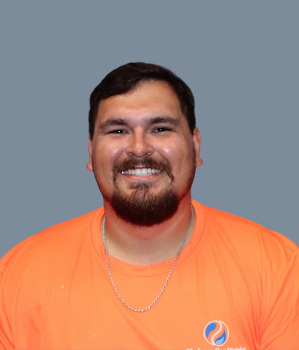The image features a smiling man wearing an orange shirt with a logo, set against a gray background.