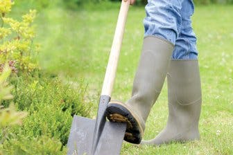 Person wearing boots using a shovel in a garden.