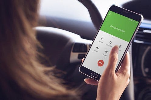 A person is holding a smartphone with the screen displaying "Emergency number" inside a car.