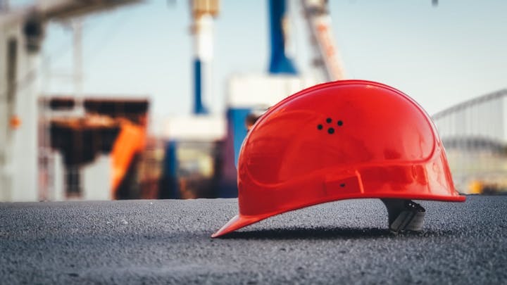 A red hard hat on the ground at a construction site, with blurred equipment in the background.