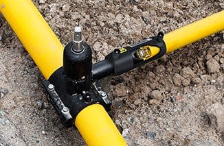 It's a yellow pipe T-joint with a black tool attached, placed on a dirt surface.
