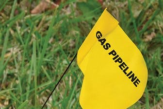 A yellow flag with "GAS PIPELINE" printed on it, placed in grass.