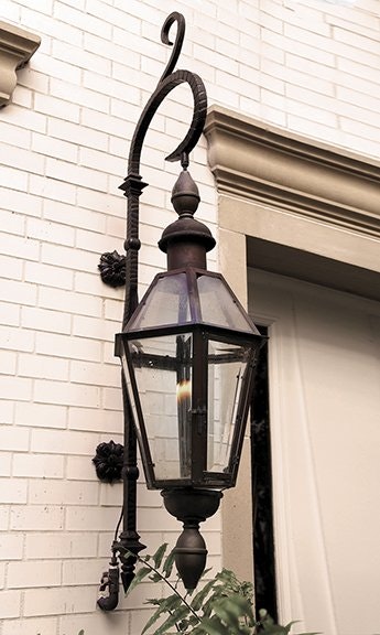A vintage-style outdoor wall lantern with glass panels mounted on a light-colored brick wall.