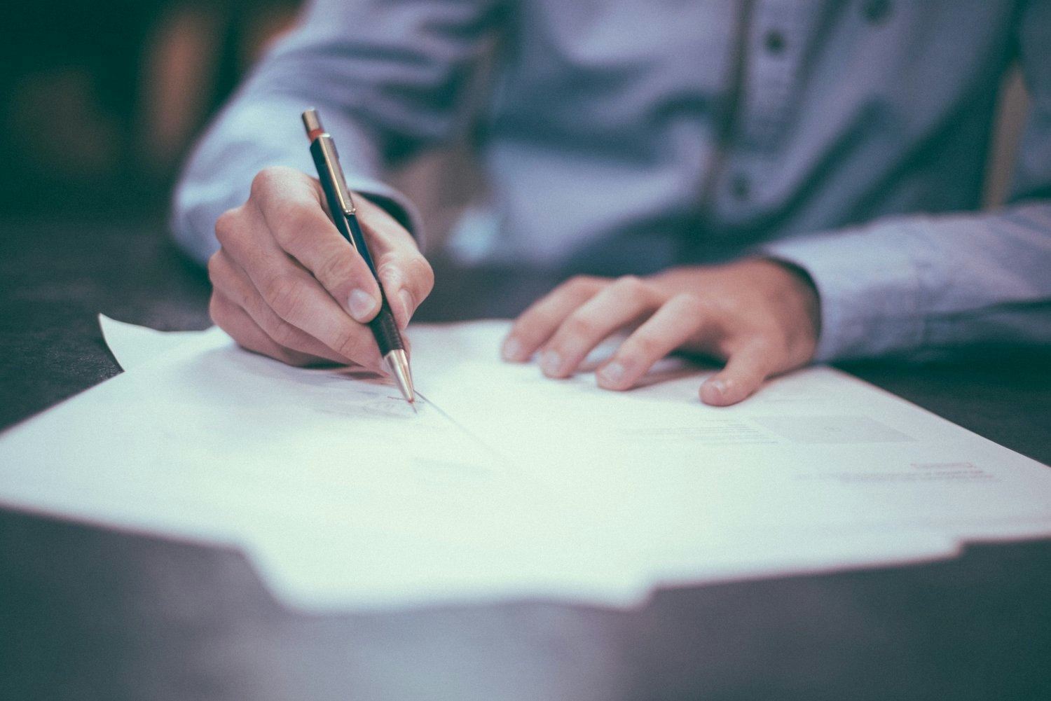 A person writing on papers with a pen, wearing a long-sleeved shirt.