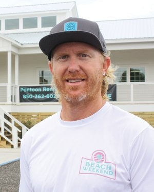 Man in a cap and "Beach Weekend" shirt standing in front of a building with a "Pontoon Rental" sign.