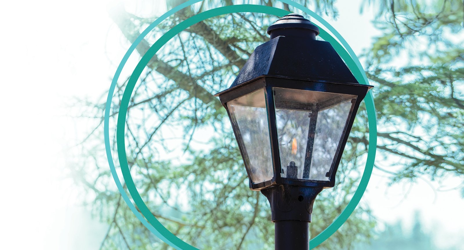 A black lantern with a glass enclosure, lit by a small flame, with trees and two overlapping teal circles in the background.