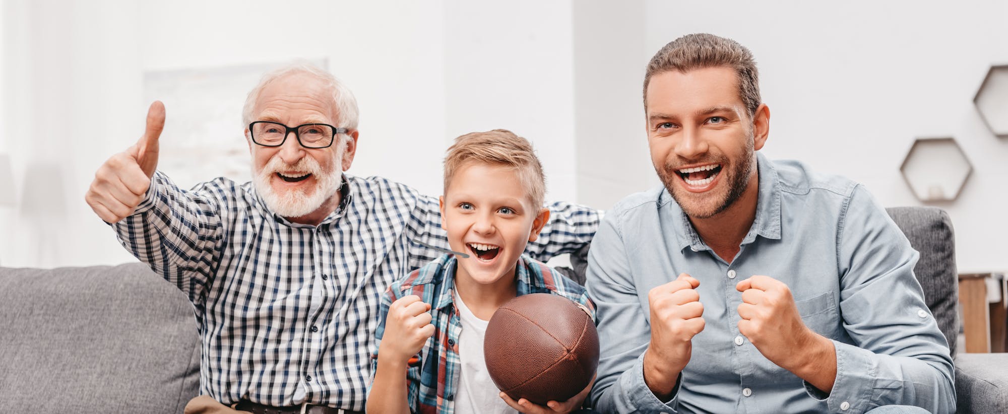 Three people excitedly watching something on TV, with a boy holding a football.