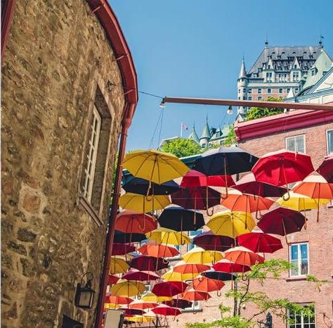 Left: A waterfall viewed from a boat with people in raincoats. Right: Colorful umbrellas hanging above a brick alley.