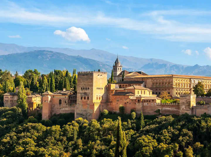 A stunning view of the Alhambra, a historic palace and fortress complex in Granada, surrounded by lush greenery and mountains.