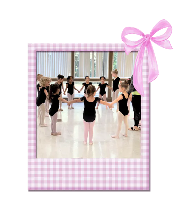 A group of young girls in ballet attire are holding hands in a circle during a dance class, captured in a charming frame.