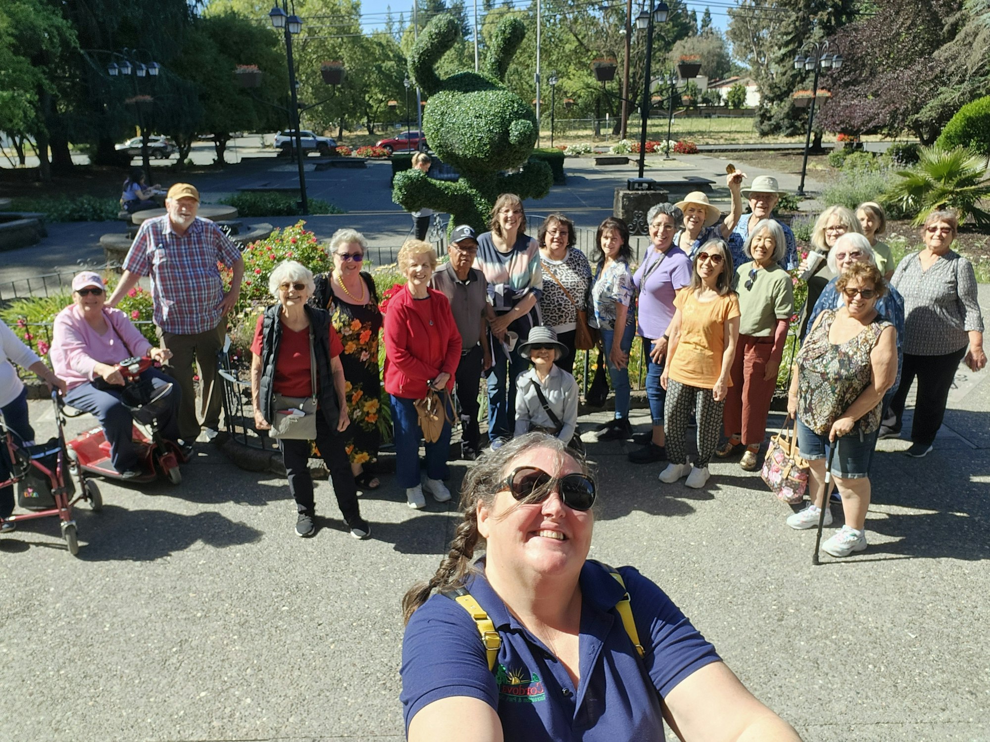 A group of people smiling for a photo in a garden with topiary animals and colorful flowers.