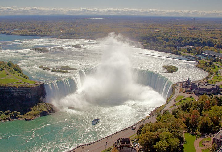Aerial view of a large, misty waterfall with surrounding greenery and a boat nearby.