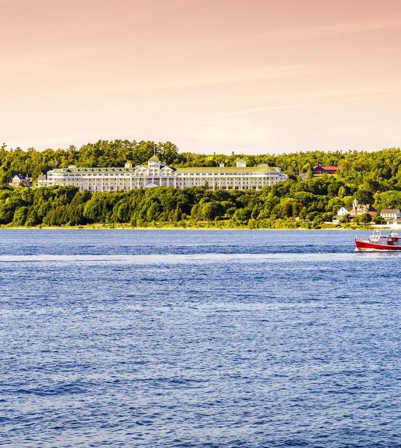 A large building surrounded by trees overlooks a body of water with a red boat.