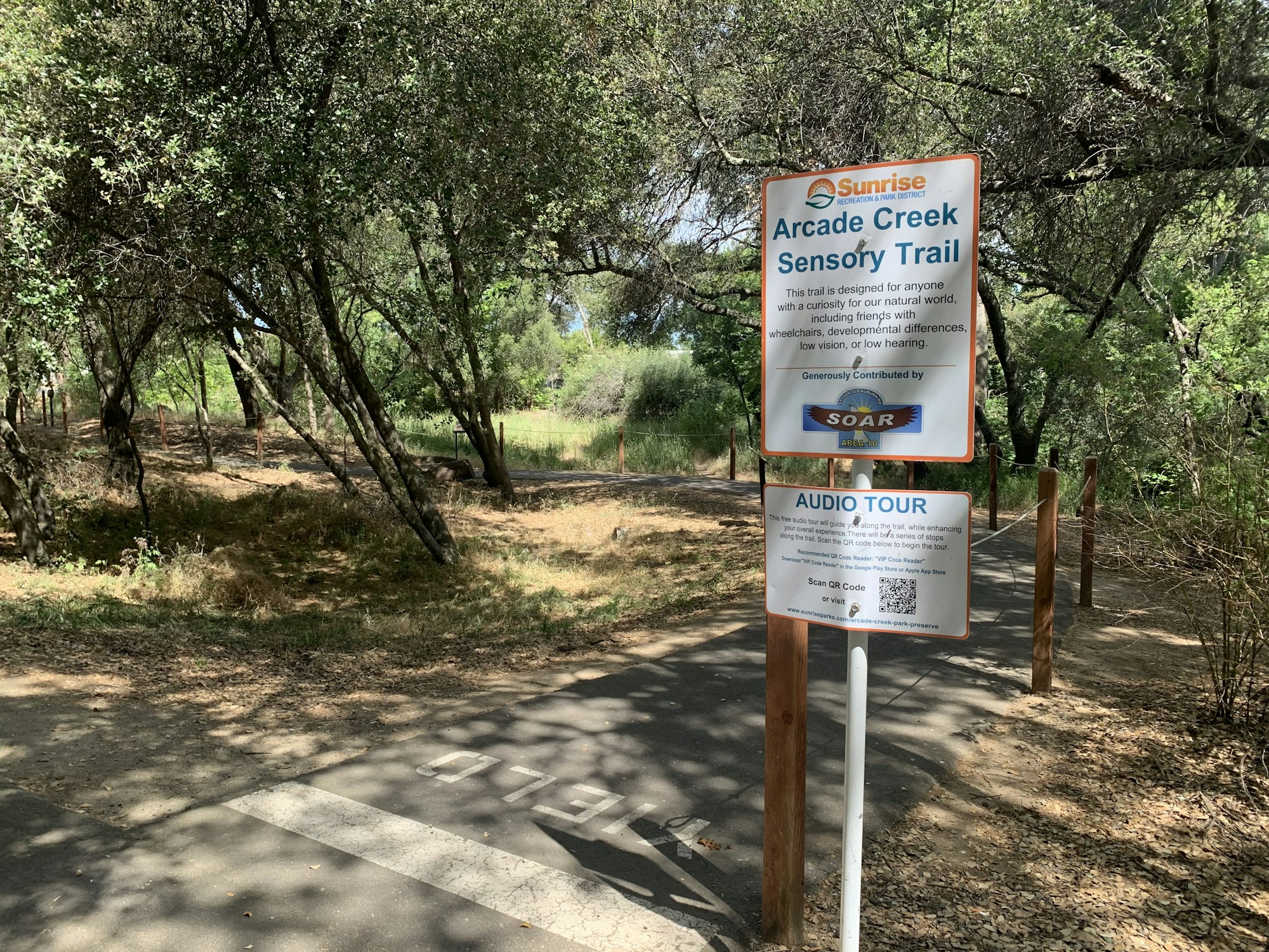 The image shows a sign for the Arcade Creek Sensory Trail, designed for diverse accessibility, including an audio tour option.