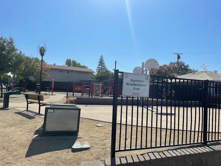The image shows a neighborhood park named "Sayonara Neighborhood Park," featuring playground equipment, benches, and a basketball hoop.