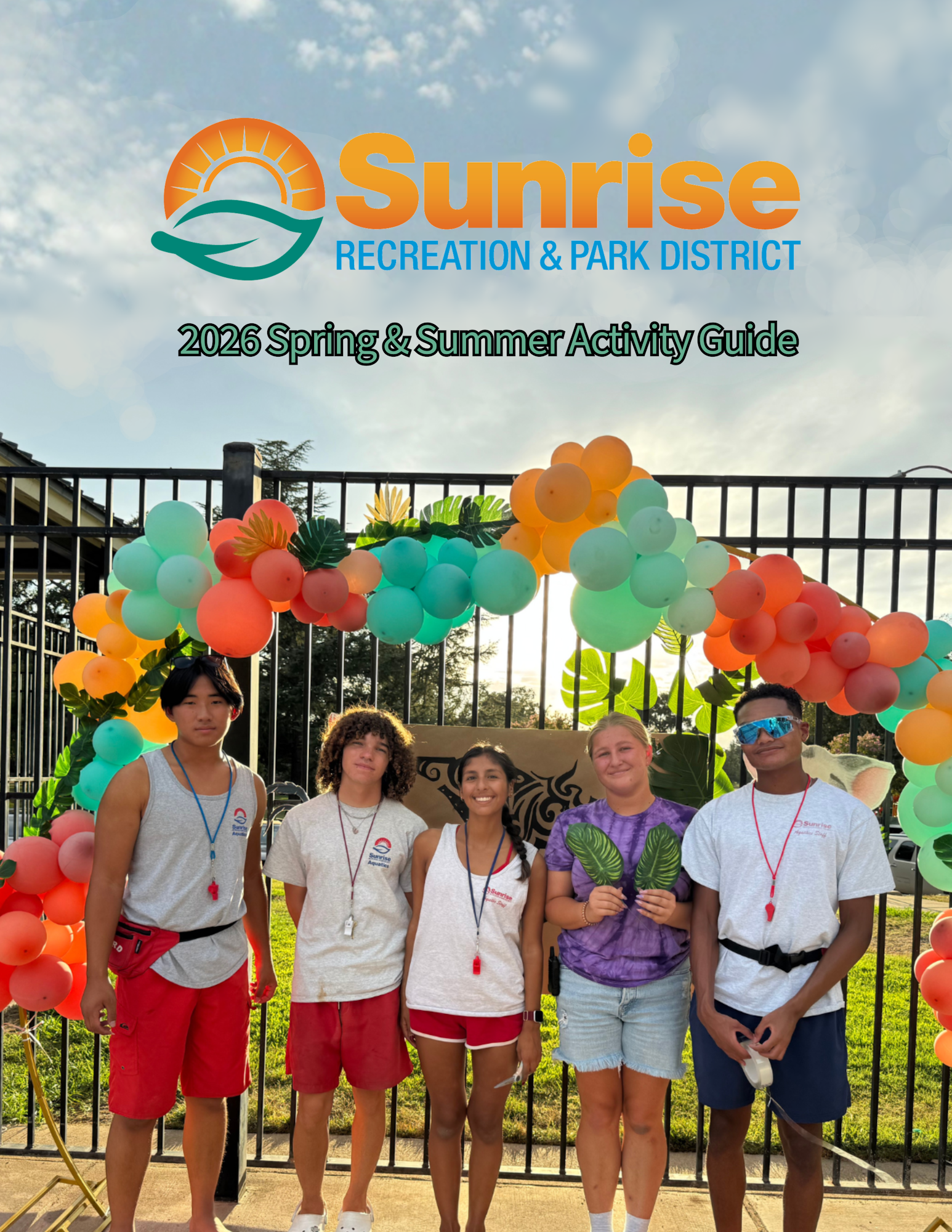 A group of five smiling individuals in casual attire standing under a colorful balloon arch for the 2026 Sunrise Recreation guide.