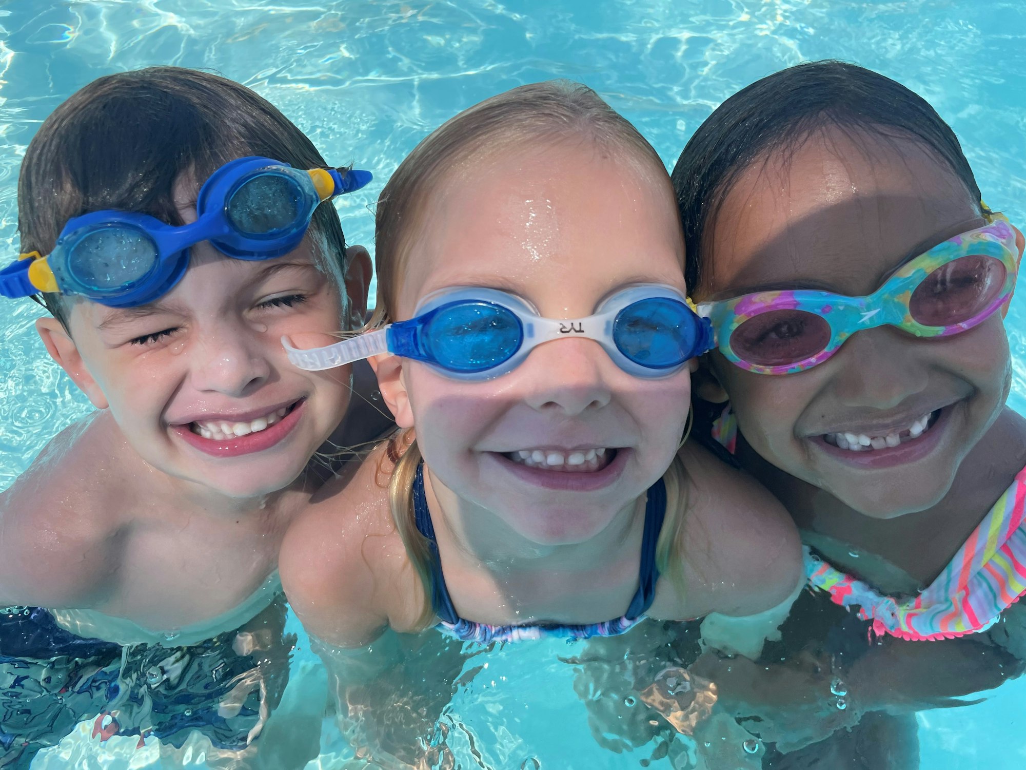 Three smiling children with goggles in a pool.