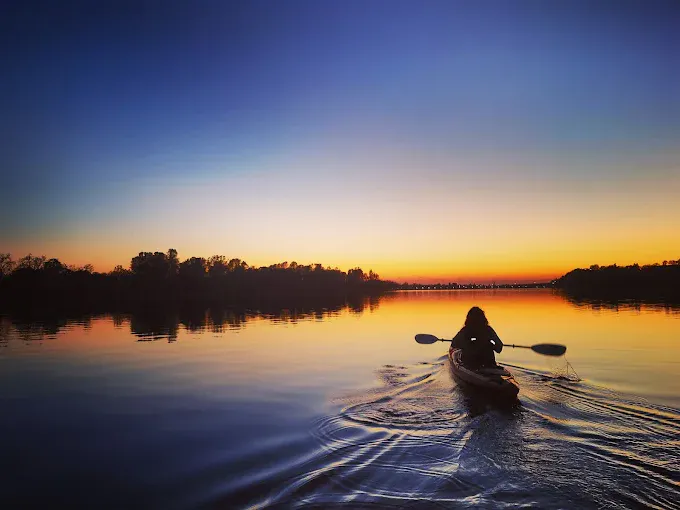 A silhouette of a person kayaking at sunset, reflecting vibrant colors on calm water.
