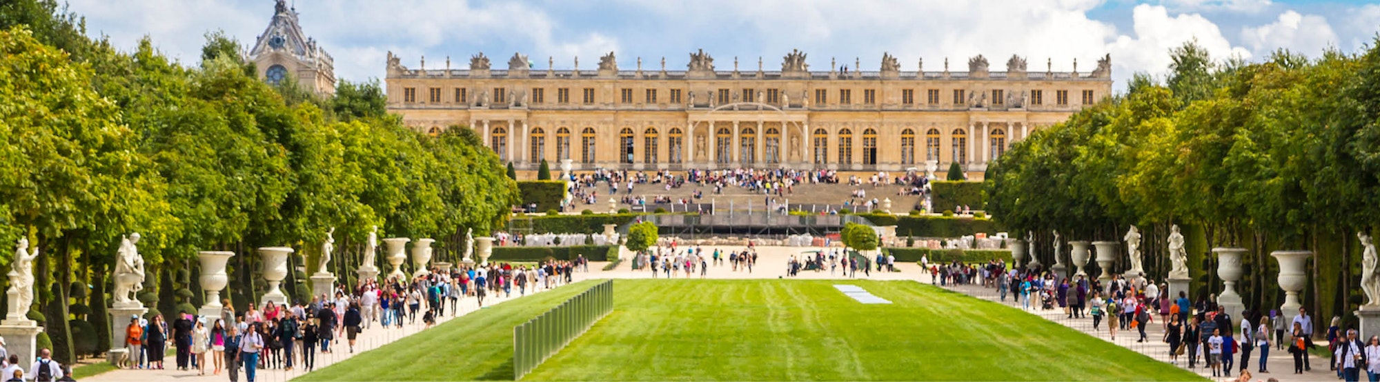 A grand palace with lush gardens and crowds of visitors enjoying a beautiful day outdoors.