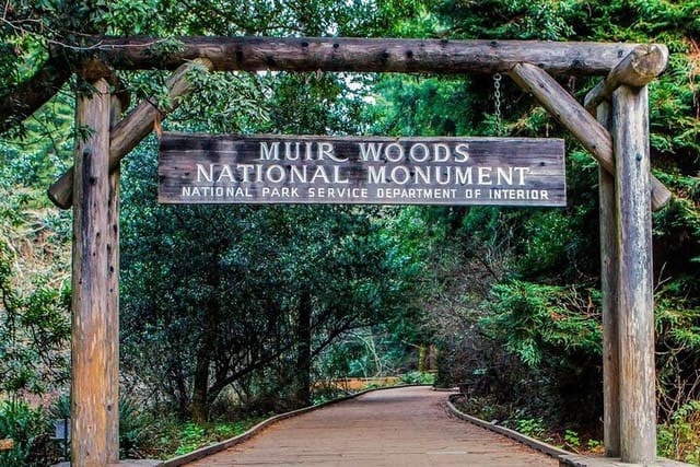 Entrance sign to Muir Woods National Monument, surrounded by lush green trees.