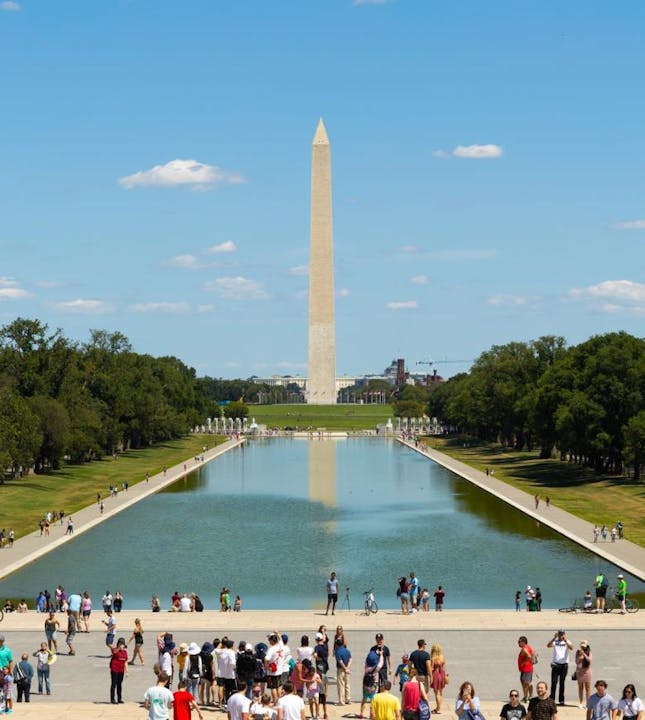 A bright day at the National Mall featuring the Washington Monument, reflecting pool, and lots of visitors enjoying the scenery.