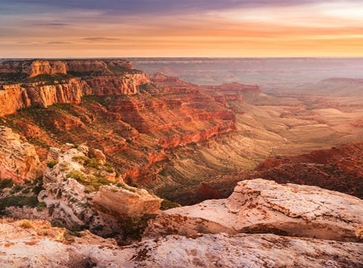 A vast canyon landscape with layered rock formations under a sunset sky.
