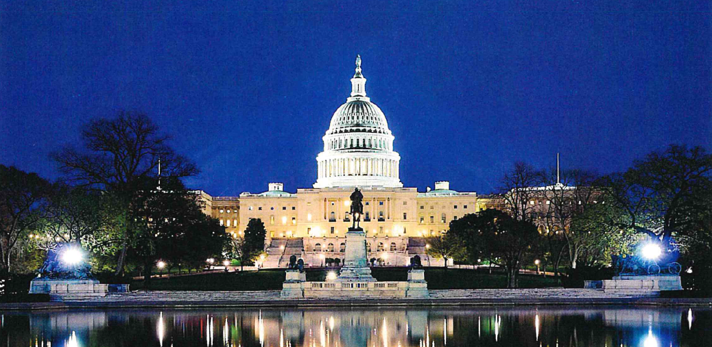 The image shows the Capitol building in Washington, D.C., illuminated at night, reflecting in a nearby body of water.