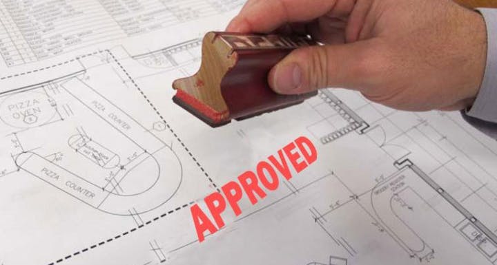 An official stamp marked "APPROVED" is placed on architectural plans for a pizza restaurant.