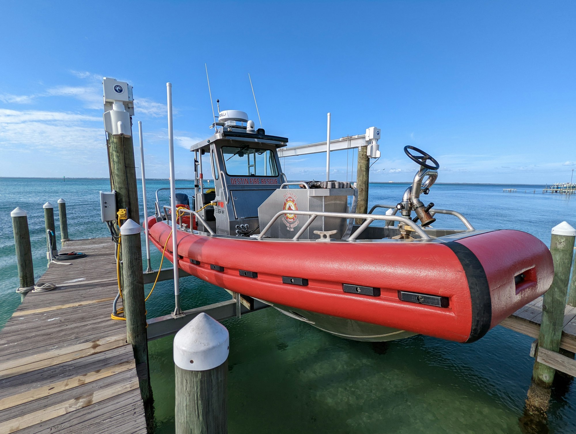 A red rescue boat docked at a wooden pier on a clear day with blue skies and calm waters.
