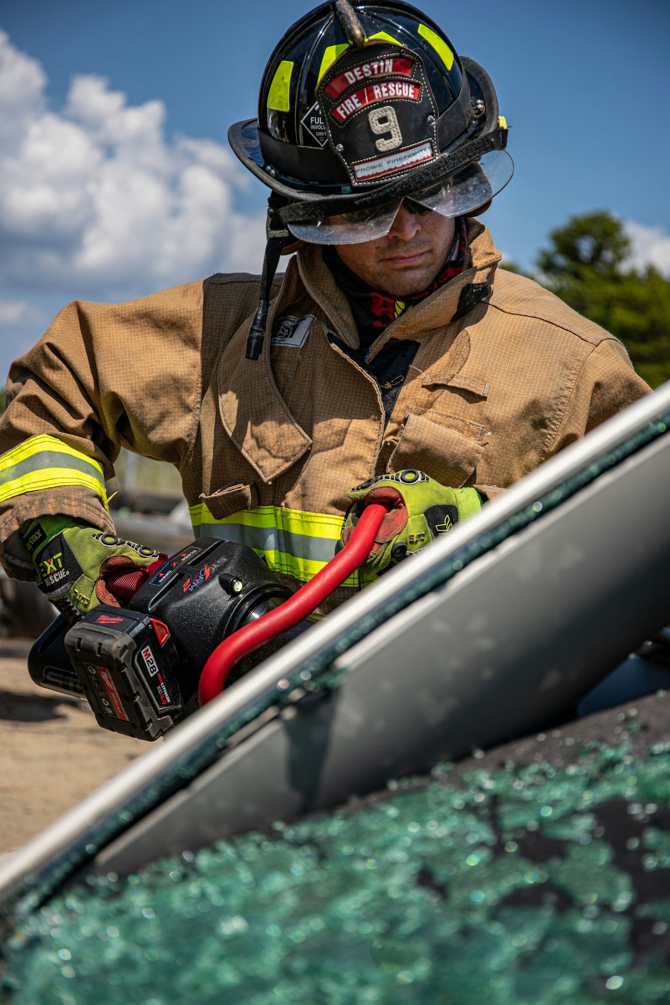 Firefighter using a power tool at a vehicle incident scene, wearing protective gear.